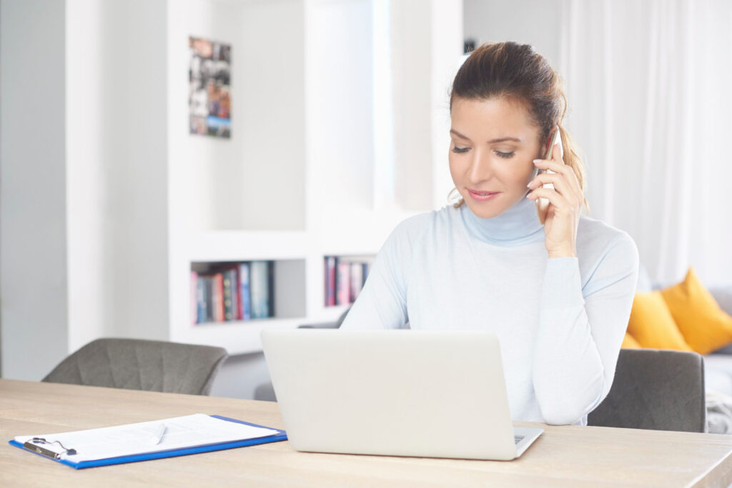 Woman speaking by phone while working at a laptop.